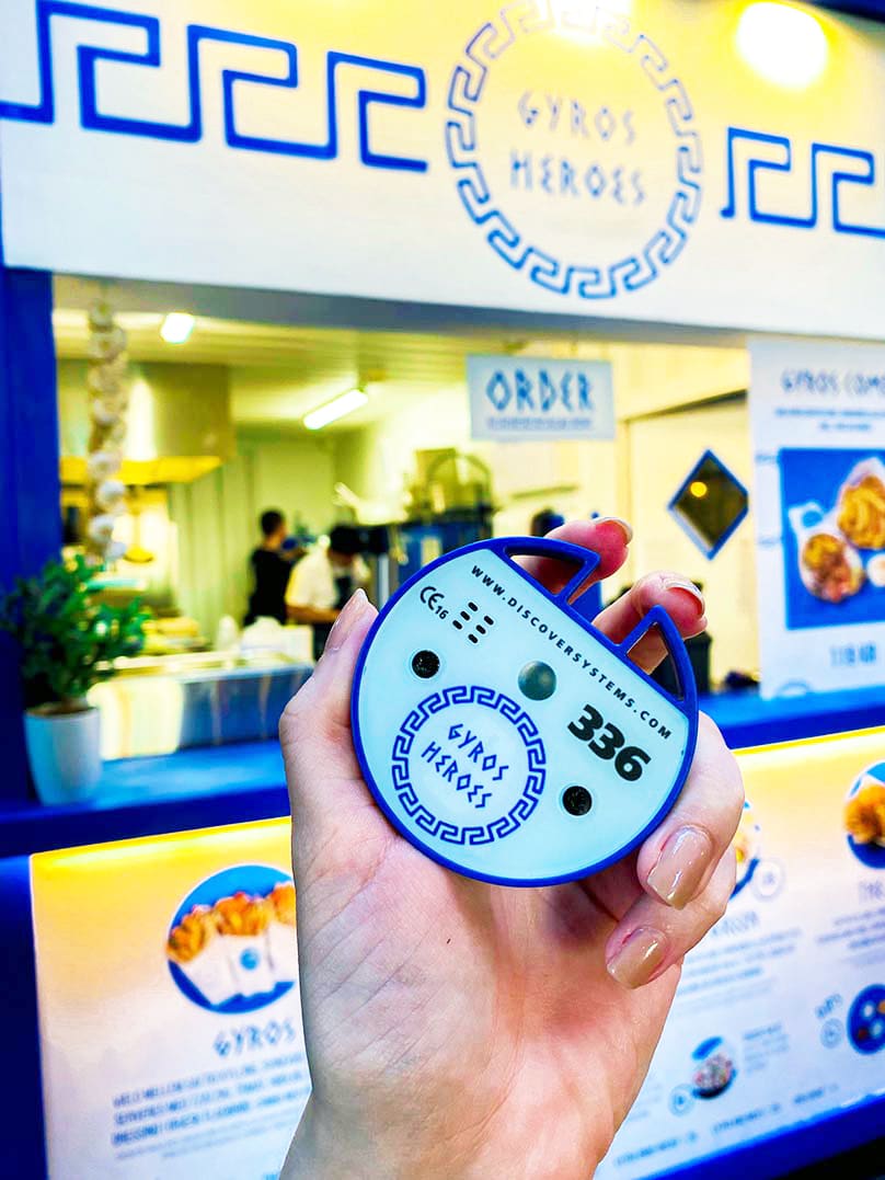 person som håller sin personsökare mot kameran med Gyros Heros i bakgrunden